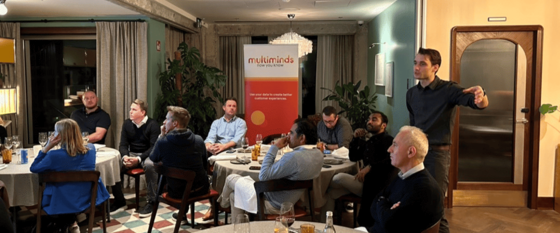 Multiminds event with attendees seated at tables and a speaker presenting.