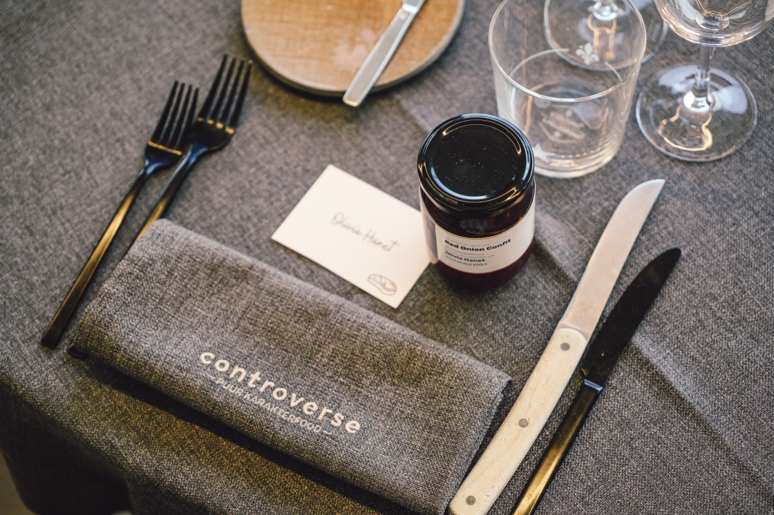 Table setting with silverware, napkin, red onion confit jar, name card, and wine glasses.