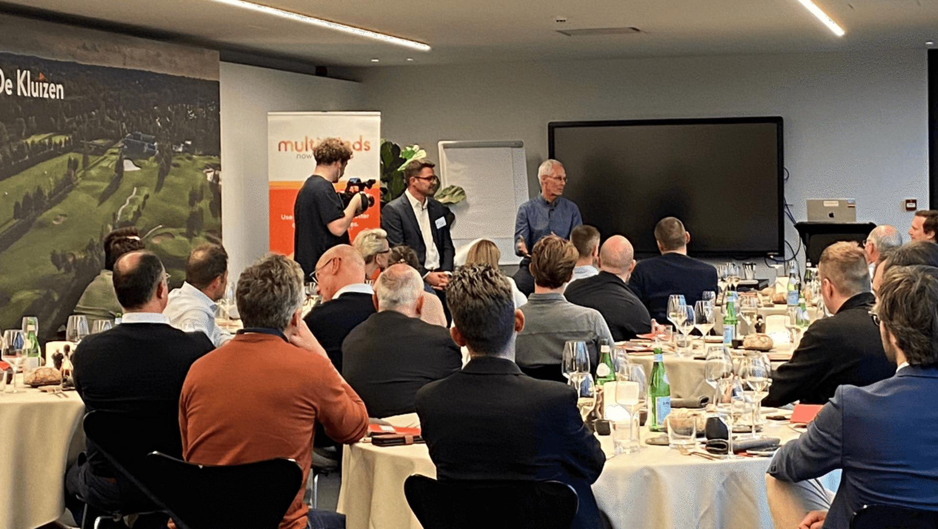 Audience attending a business presentation, with two speakers and a videographer at the front.