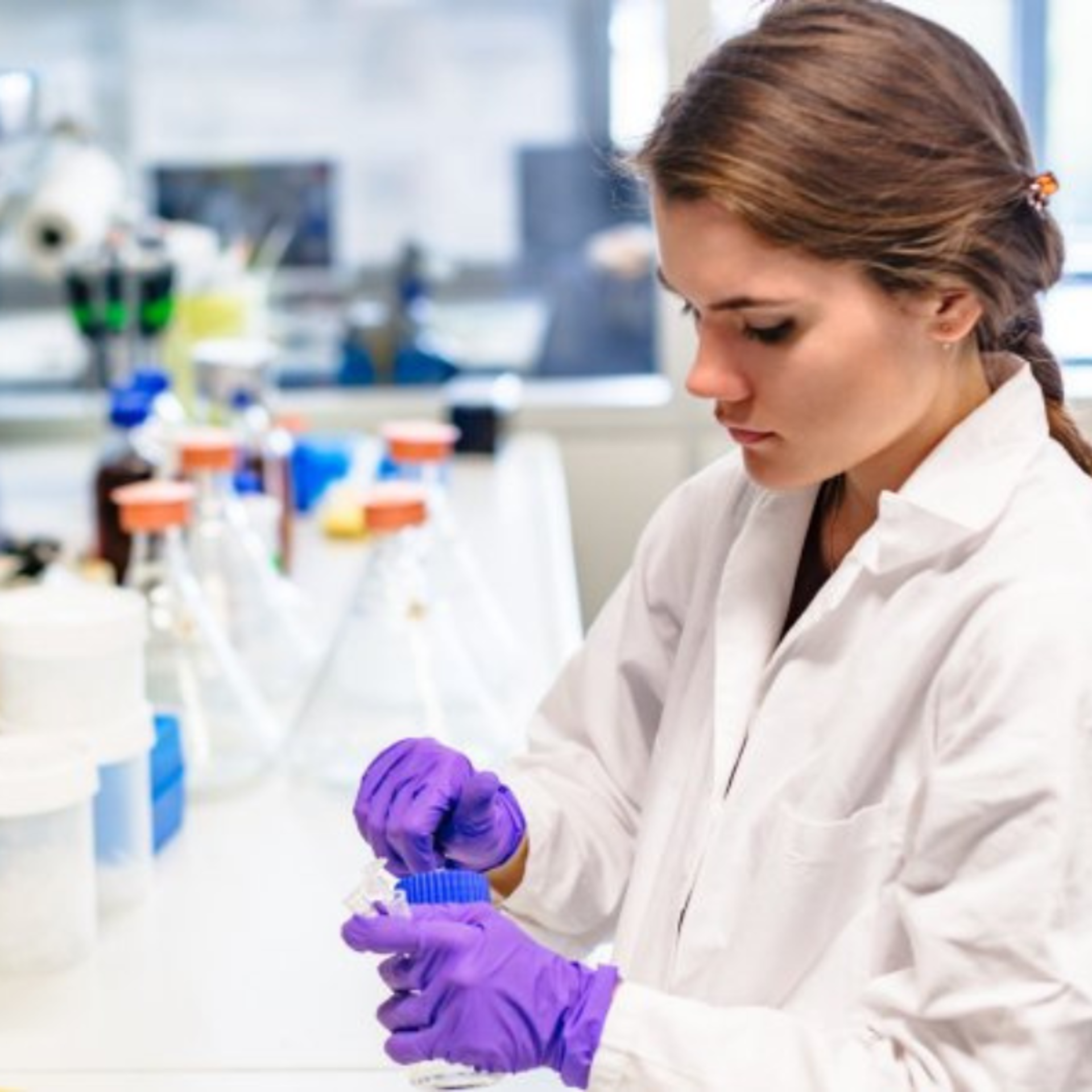 Scientist in a lab coat and purple gloves opening a chemical bottle.