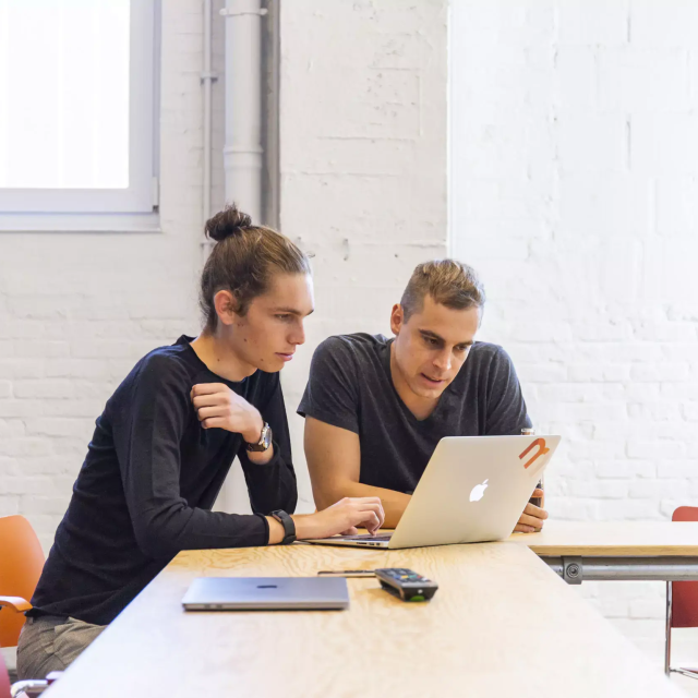 Two colleagues sitting at a desk and collaborating on a laptop in a modern office.