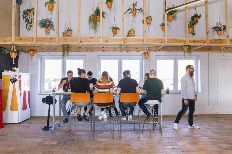 People eating and drinking at a tall table with hanging plants in a bright room.